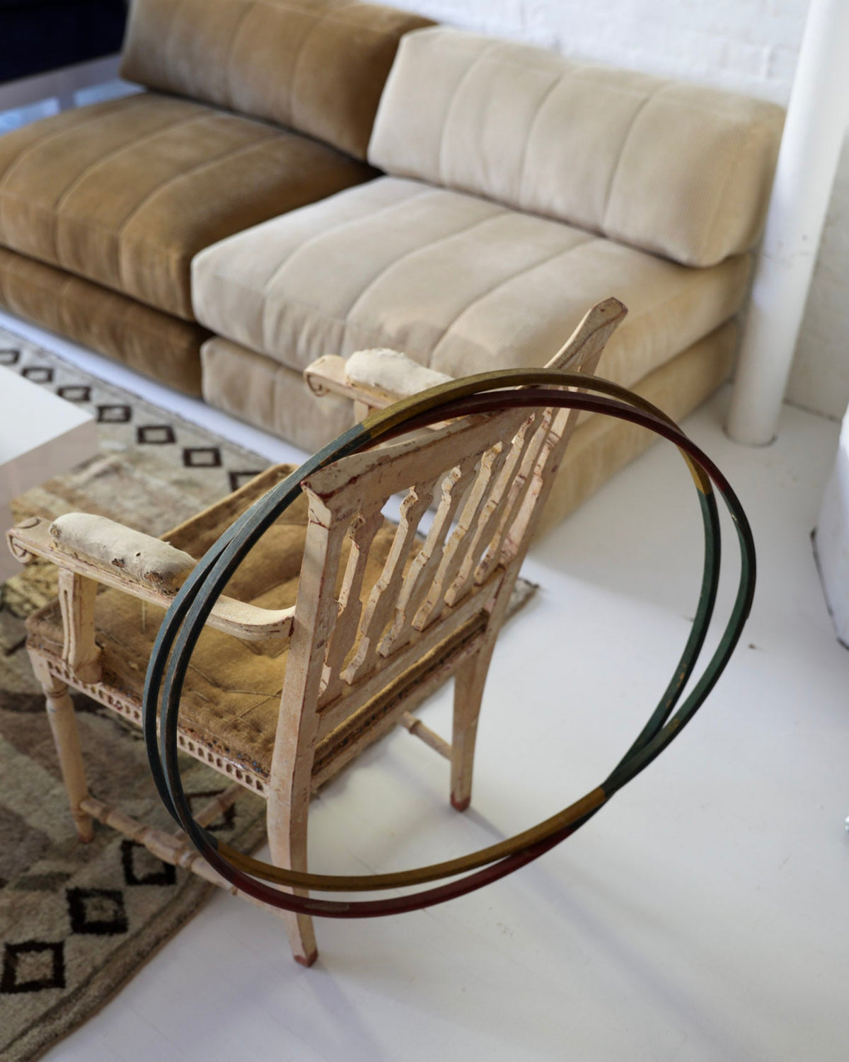 A rustic wooden chair with a woven seat and backrest, featuring a large, overlapping set of dark metal hoops wrapped around its back, set in a modern living room with a beige sofa in the background.