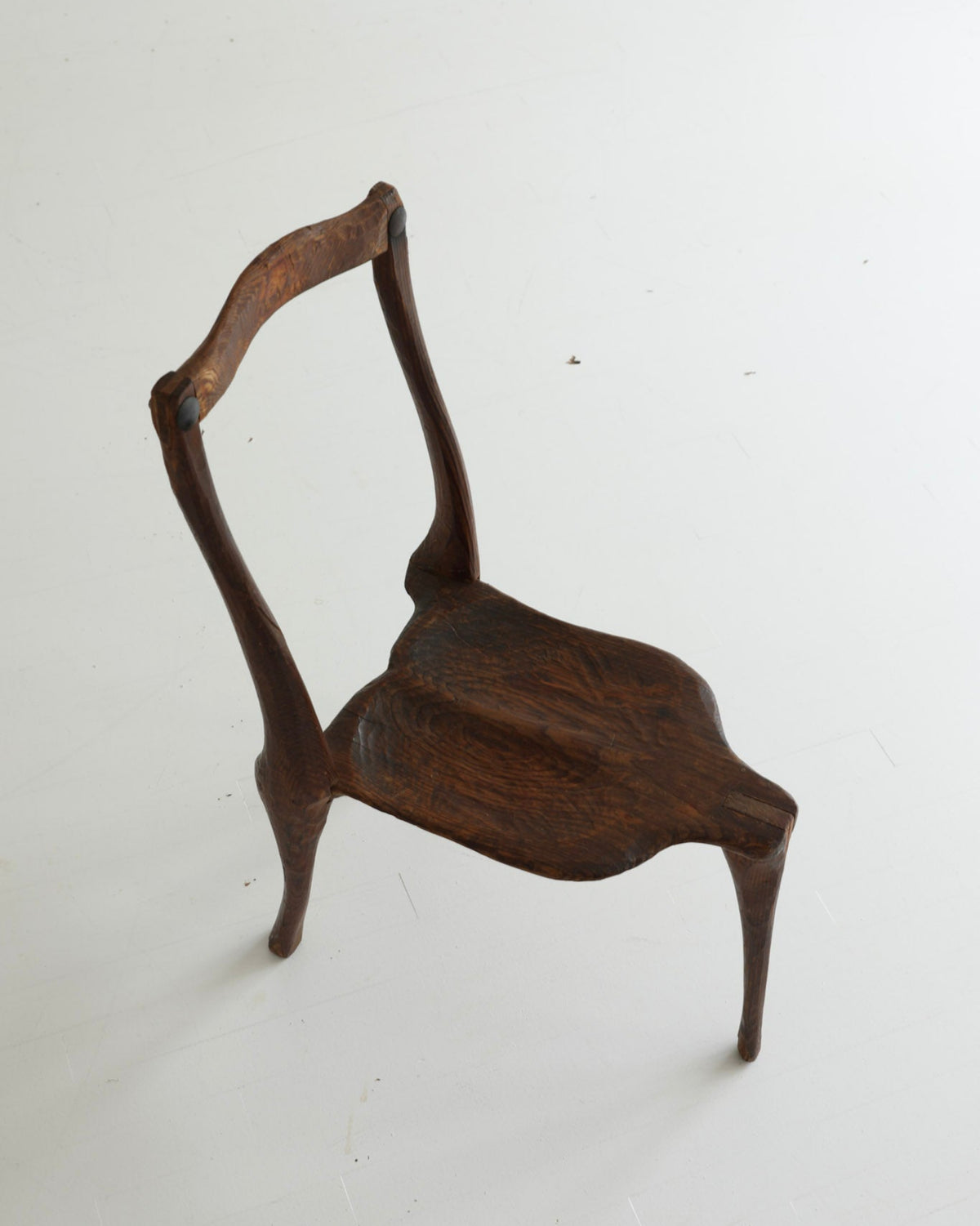 A small dark brown wooden chair with a curved backrest and splayed legs, photographed on a plain white floor.