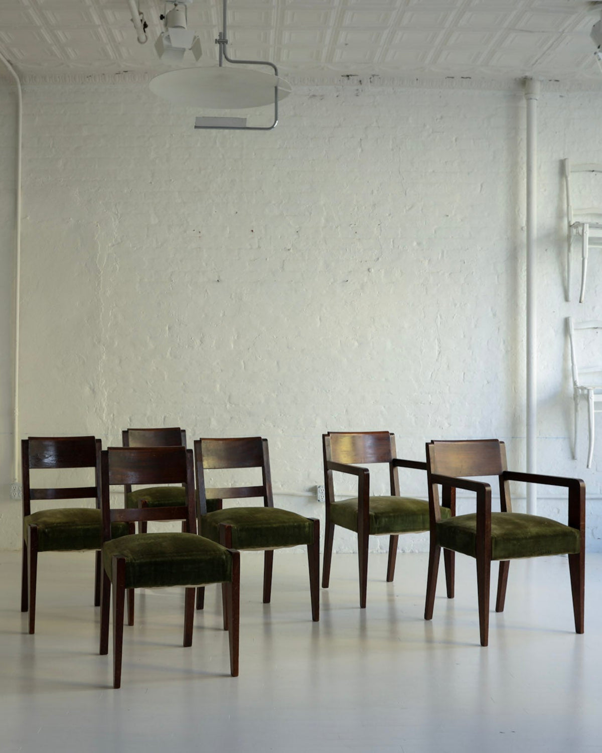 A group of six mid-century modern armchairs with dark wood frames and olive green velvet seats arranged in a minimalist white studio room.